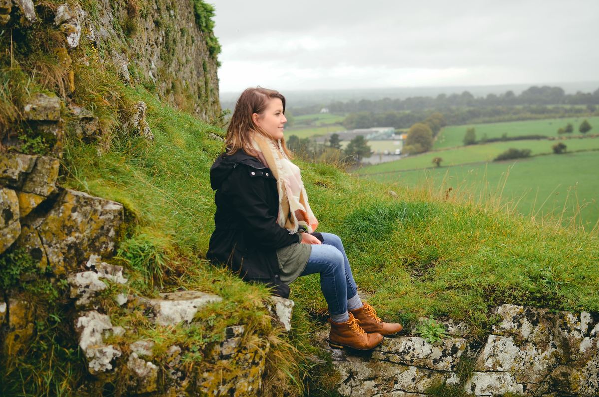a girl sitting on a grassy hill in ireland