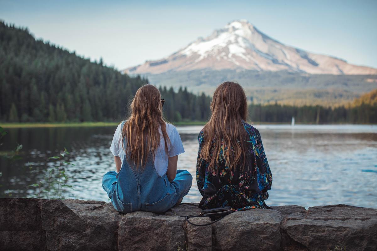 two girls sitting on water's edge looking at mountain