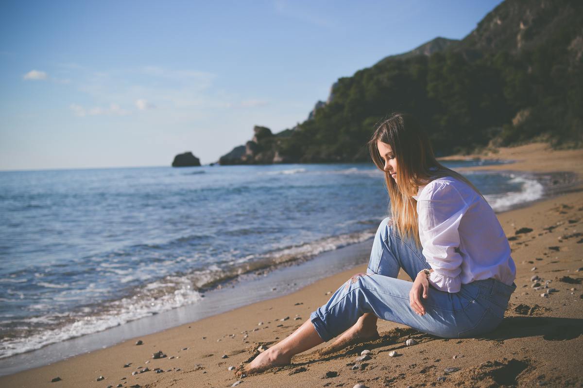 girl alone sitting on beach looking at water