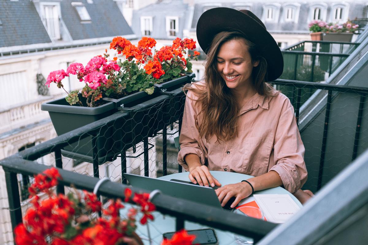woman smiling at laptop sitting outside on balcony