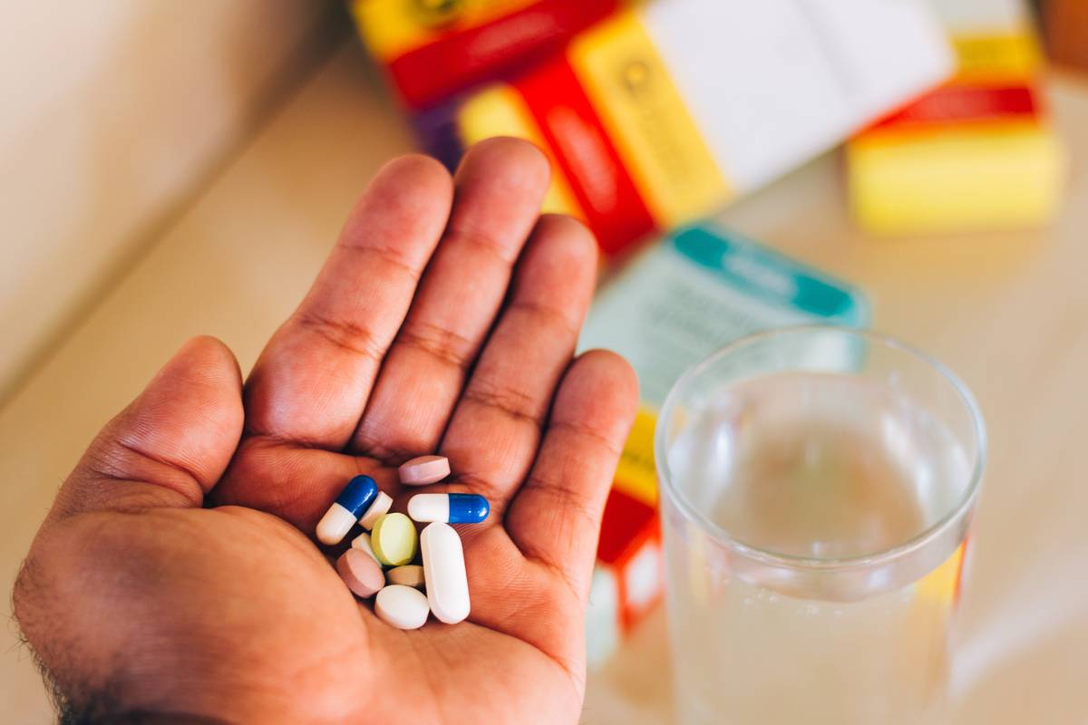 A person holds antibiotics next to a glass of water.