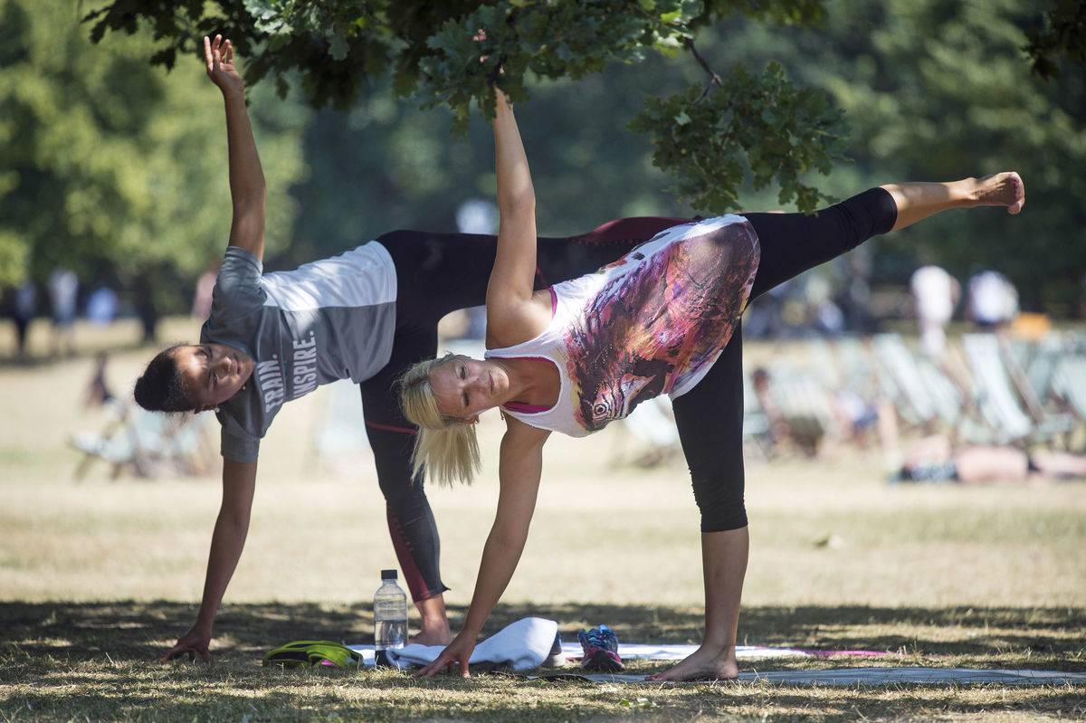 Two women perform yoga exercises in a shaded park spot.