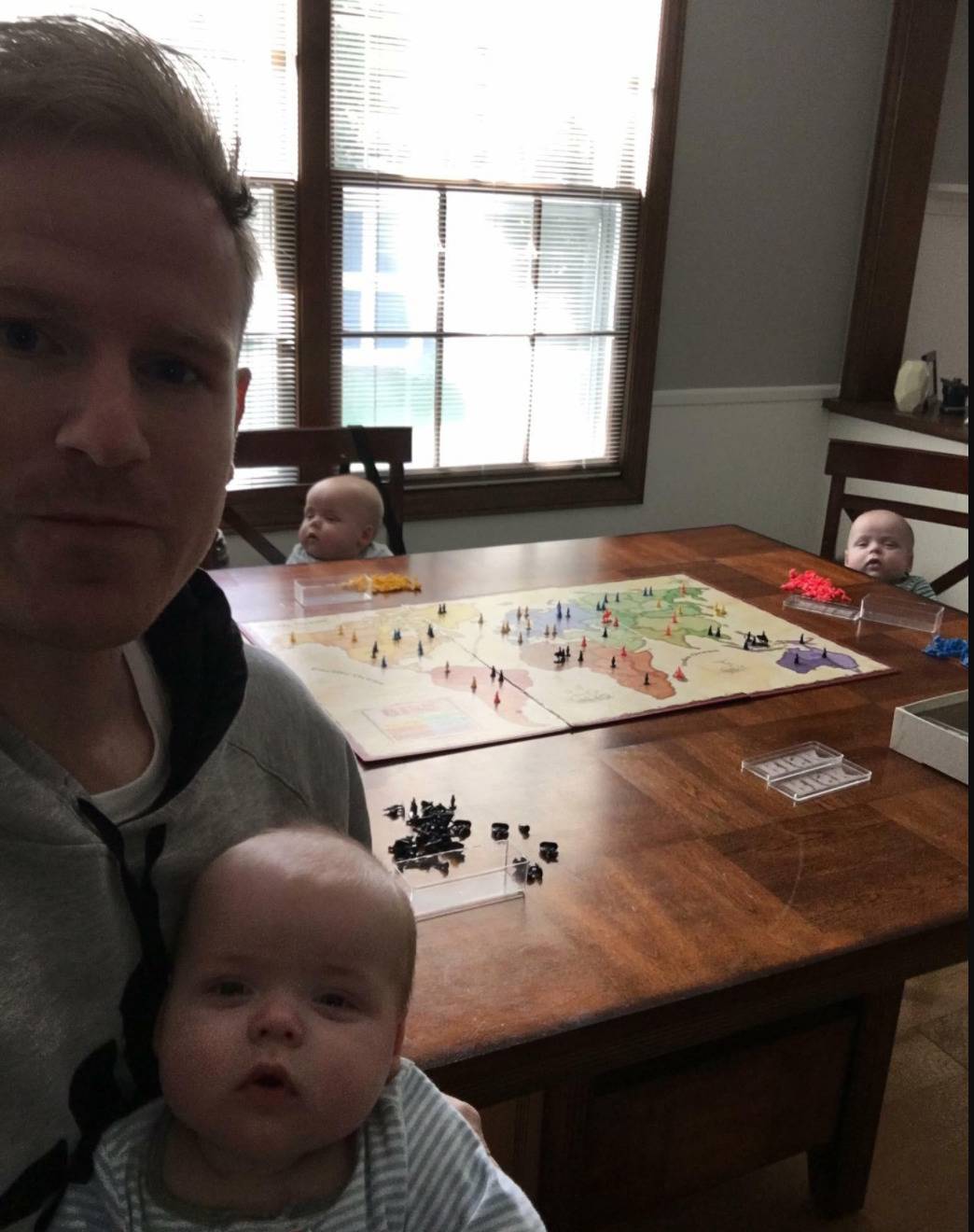 photo of dad with a baby in his arms and two babies at other seats around the dining table playing a board game