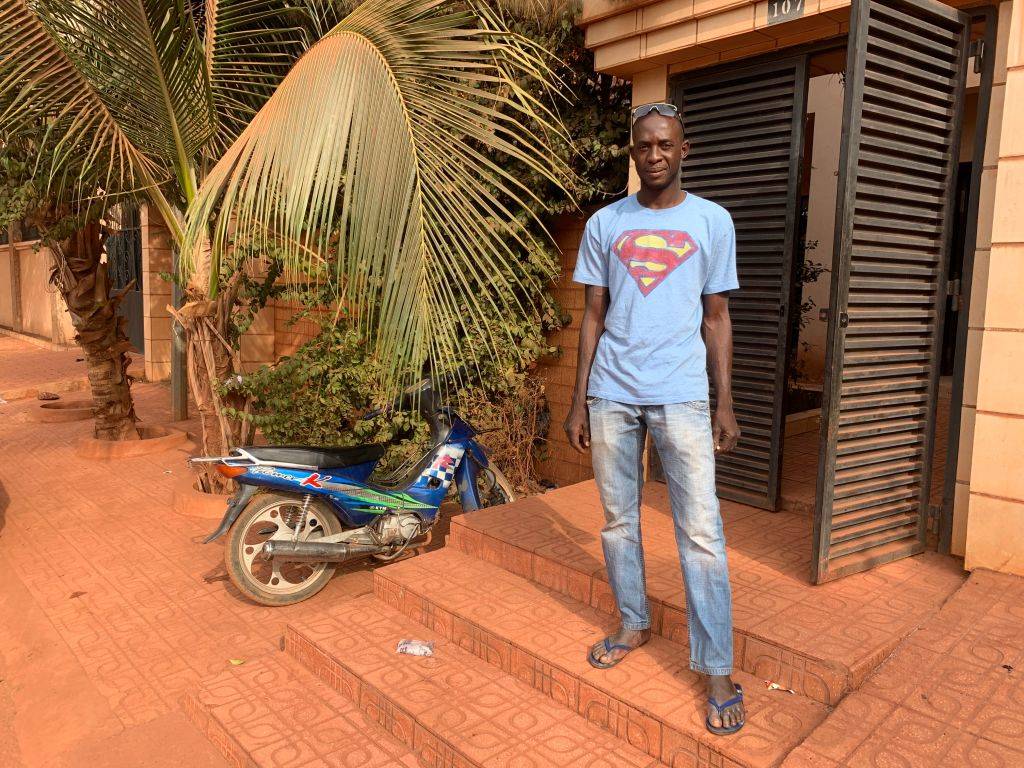 a man with a superman shirt standing near a motorcycle in bamako, mali