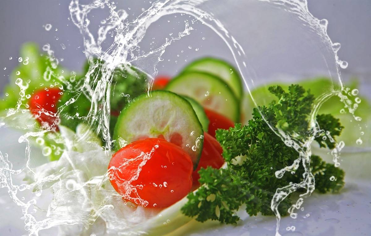 Cucumber, parsley, tomatoes, and lettuce are washed in water.