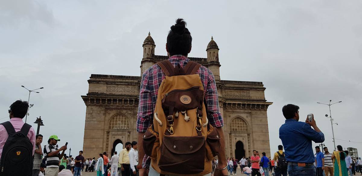 a man with a bun and backpack looking at a historic building in mumbai, india