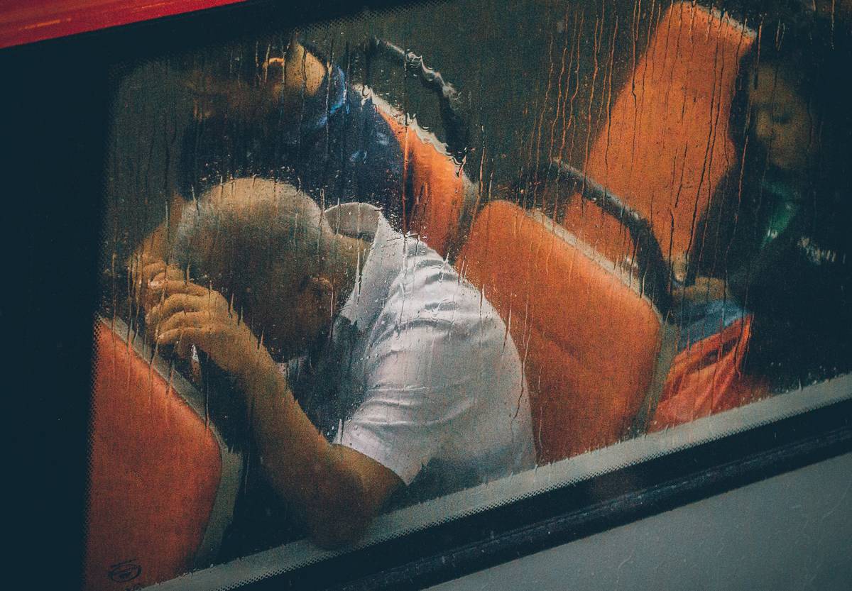 A man on a bus leans his head against the back seat.