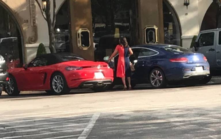woman with half red, half blue dress standing between two cars of the same shades 