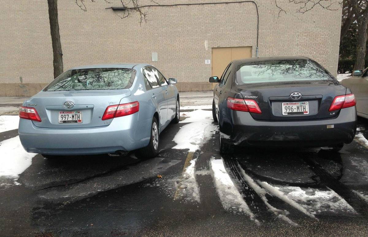 two cars of the same model parked next to each other have nearly identical license plates (one number difference)