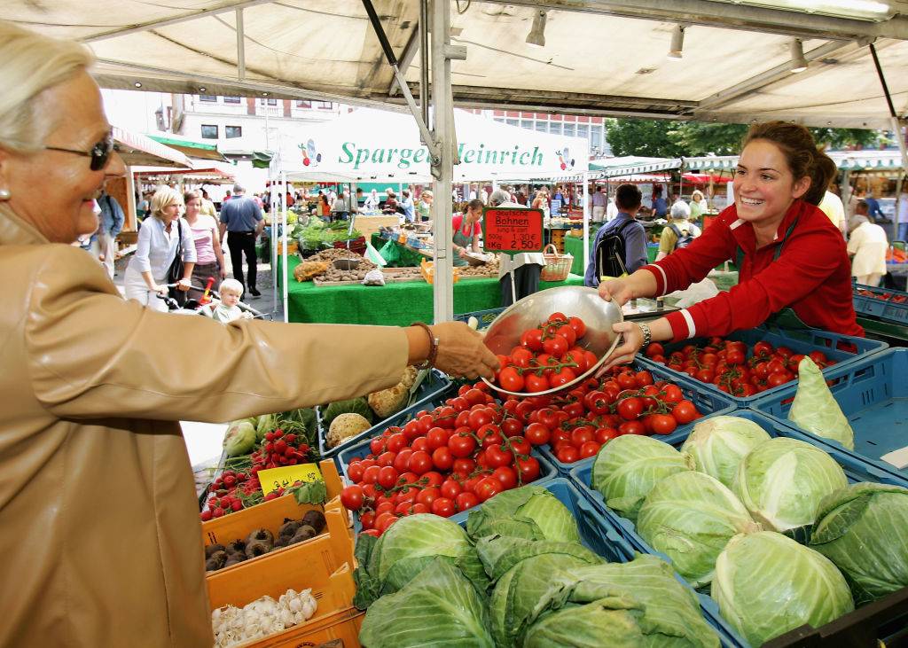 a woman giving another woman tomatoes at a farmer's market