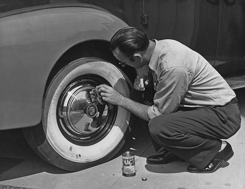 A man polishing the hubcaps of a Cadillac car