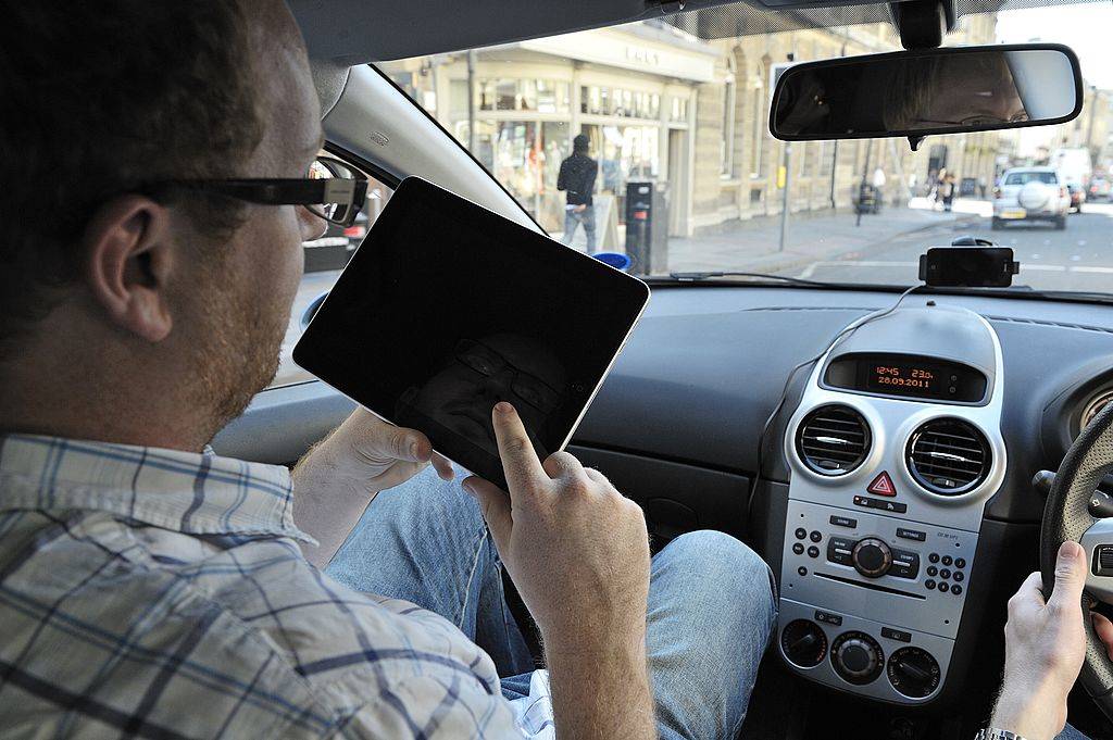 A man using an Apple iPad tablet computer whilst sitting in a car