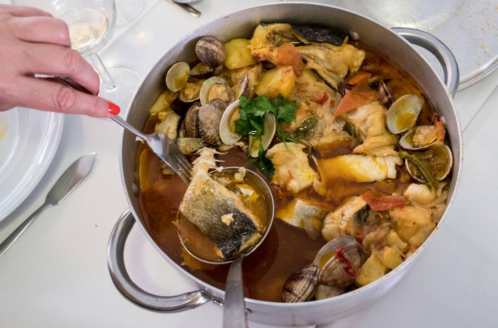 a soup with fish, potatoes, herbs, and seafood