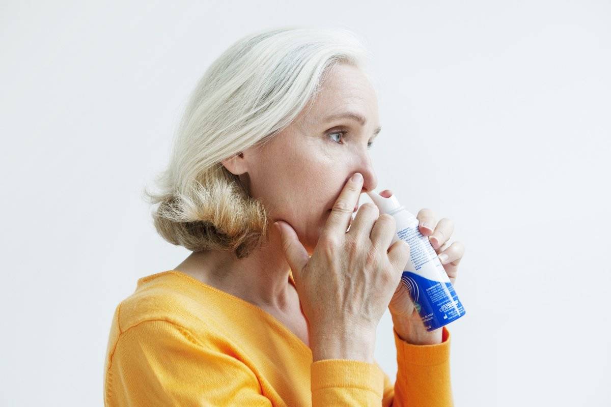 A woman sprays a decongestant into her nose.