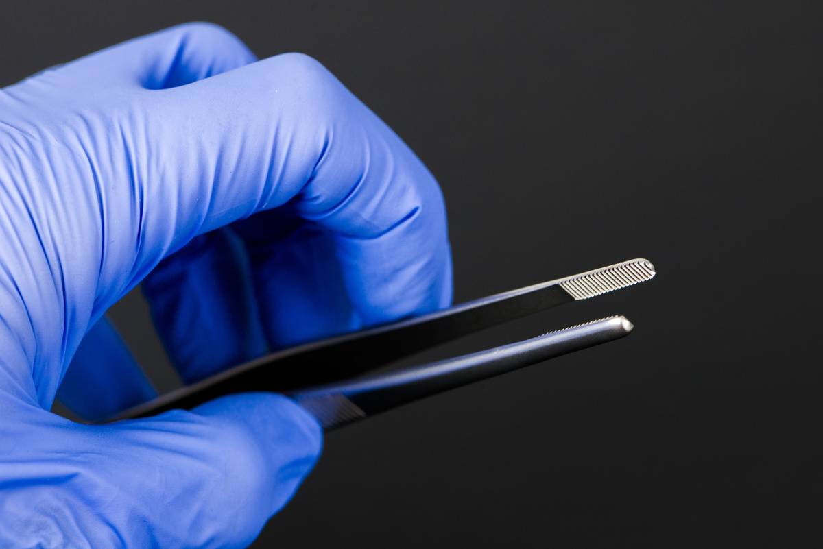 A person wearing gloves holds black tweezers.
