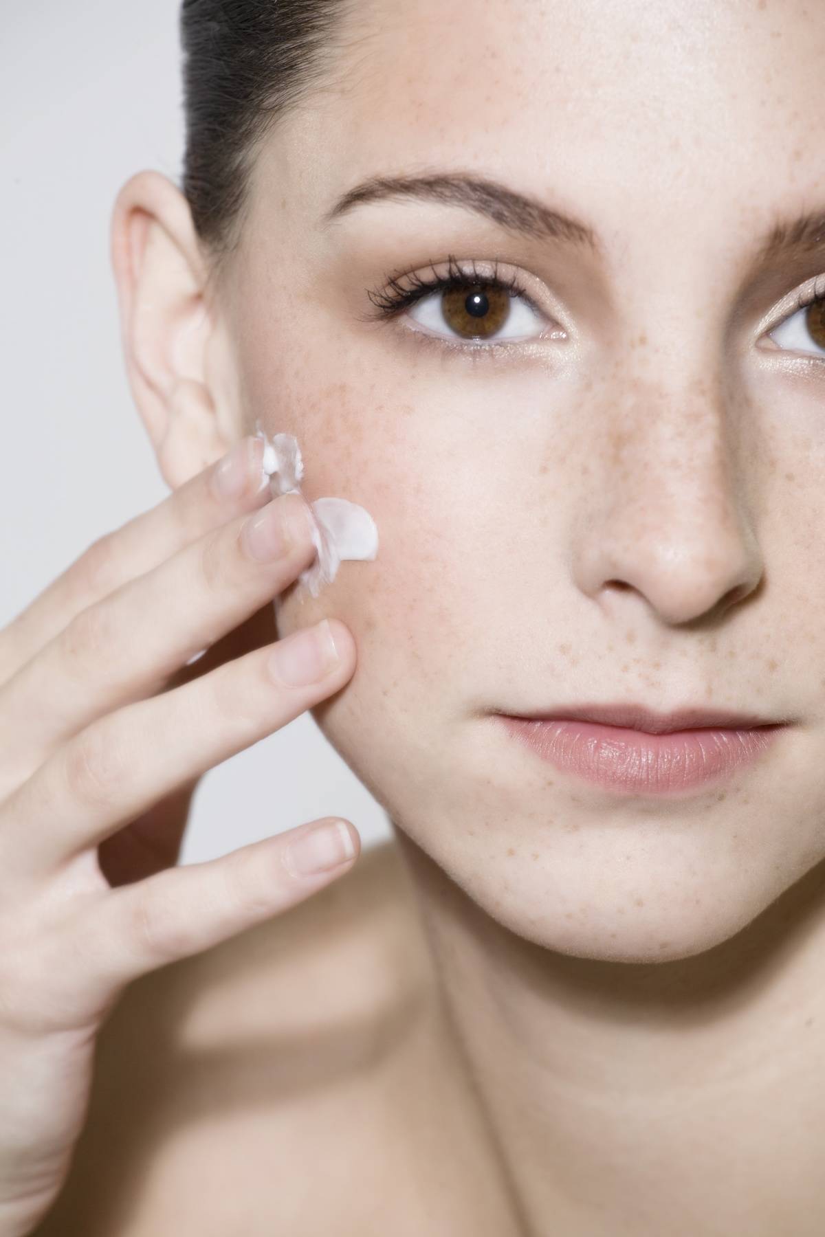A woman applies face lotion.