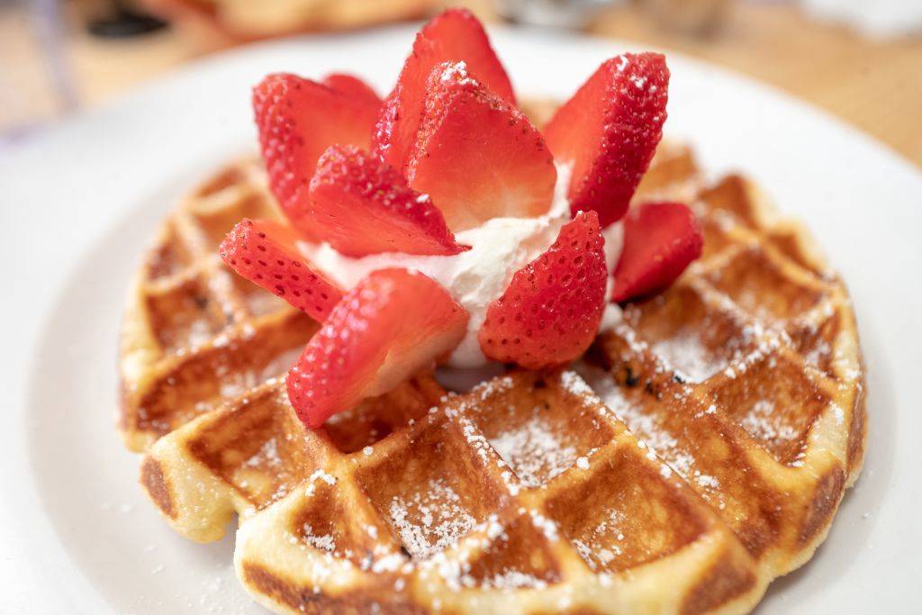 Close-up of Belgian waffle with strawberries and whipped cream on white plate