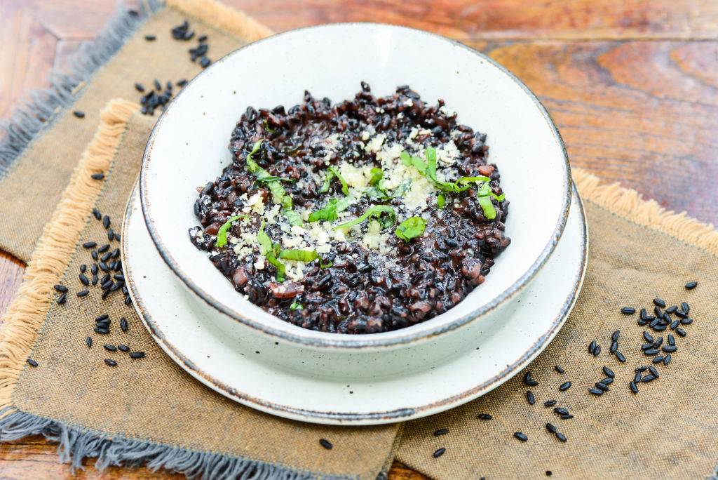 black risotto in a white bowl topped with herbs