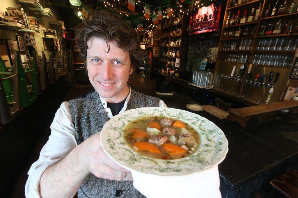 a chef holding up an irish stew of meat, carrots, and potatoes
