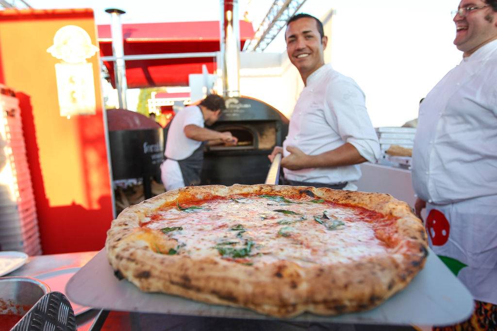 a chef taking a cheese pizza out of an oven