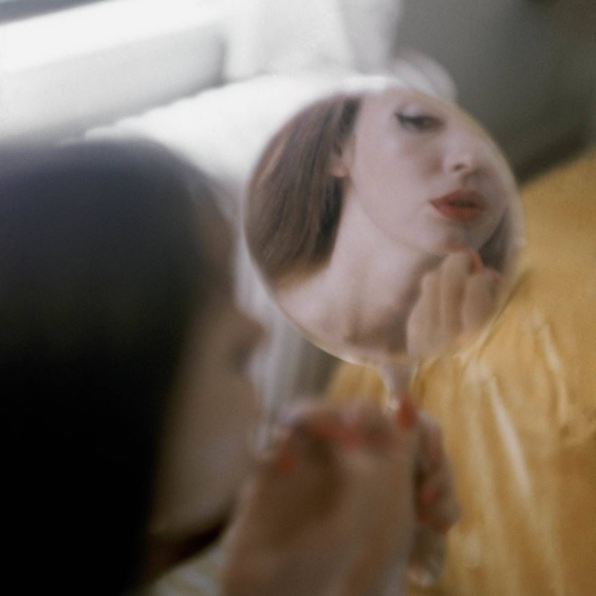 Model looking into hand mirror, applying lipstick