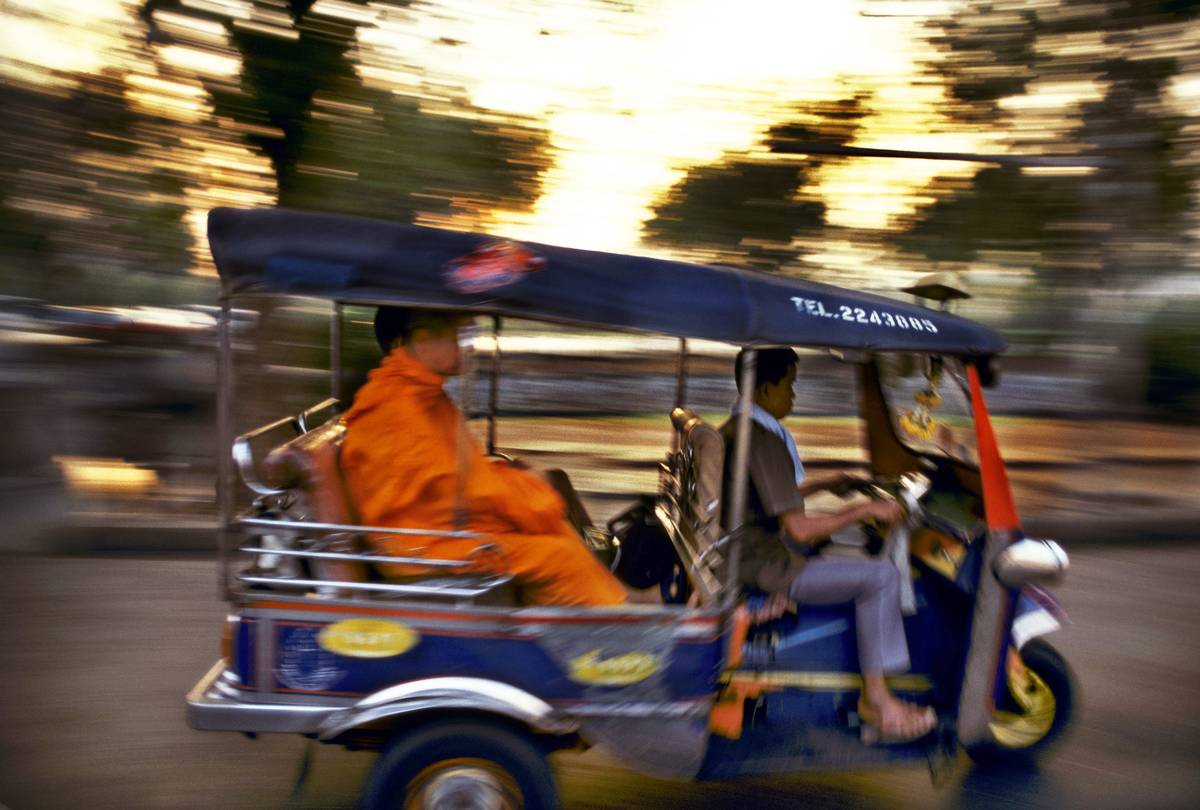 Buddhist monk in the back of a three wheel tuk tuk taxi on a road in Bangkok