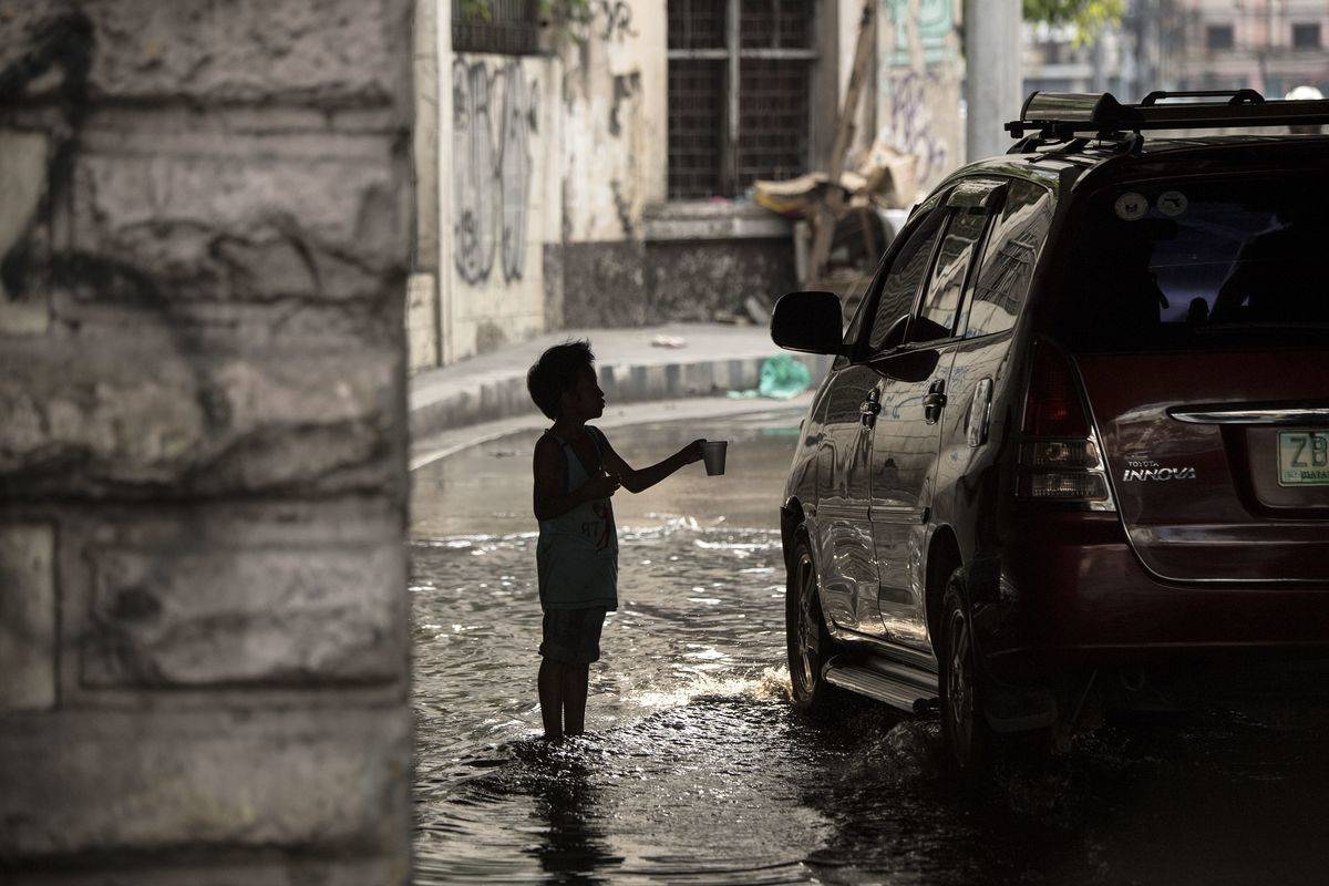 A boy is silhouetted as he asks for alms from commuters