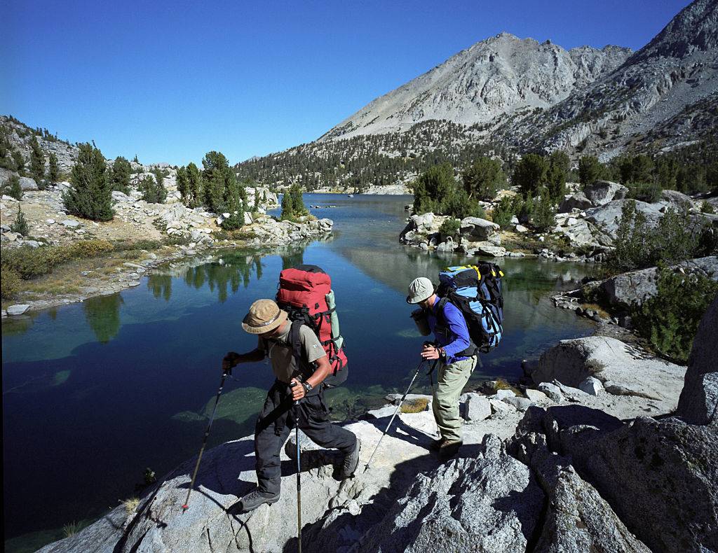 backpackers crossing over a rock near a lake on the john muir trail in california