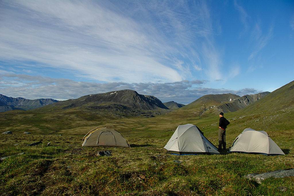 a man standing next to three tents in kesugi ridge in denali state park