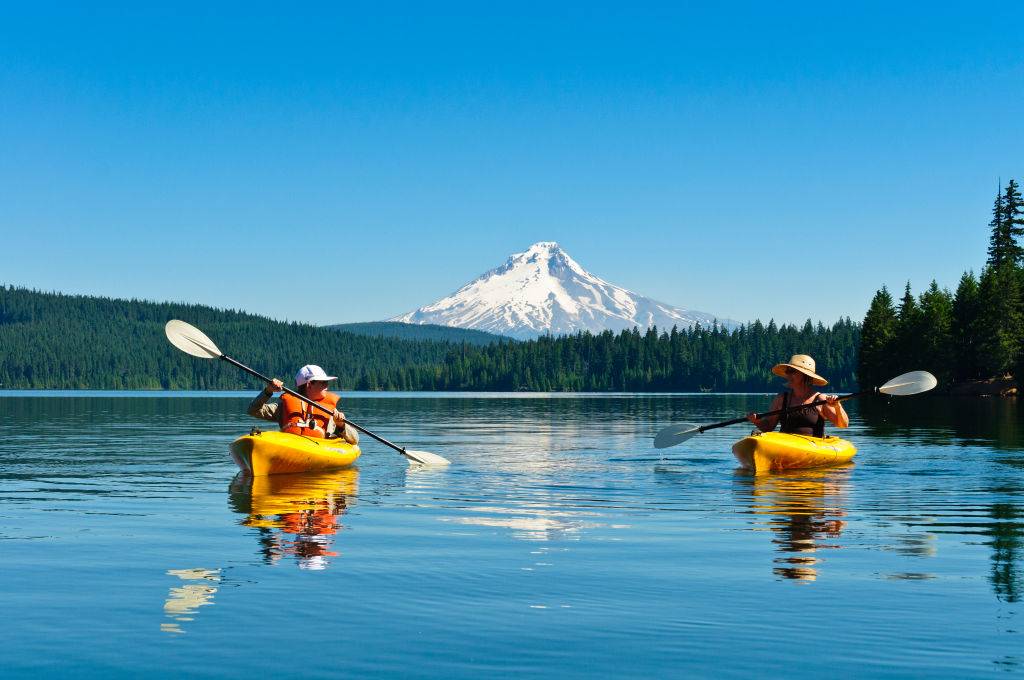 people kayaking in a lake in front of a forest and mountain in mount hood national forest in oregon