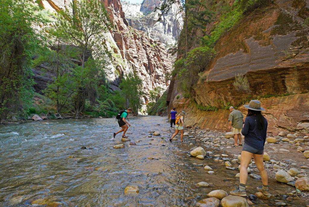 backpackers stepping across stones in the water at zion national park