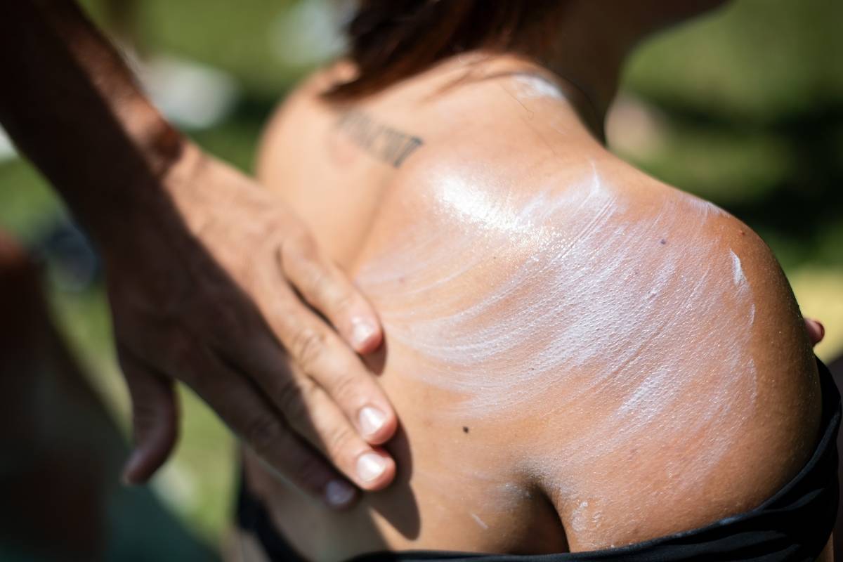 A person rubs sunscreen on a woman's back.