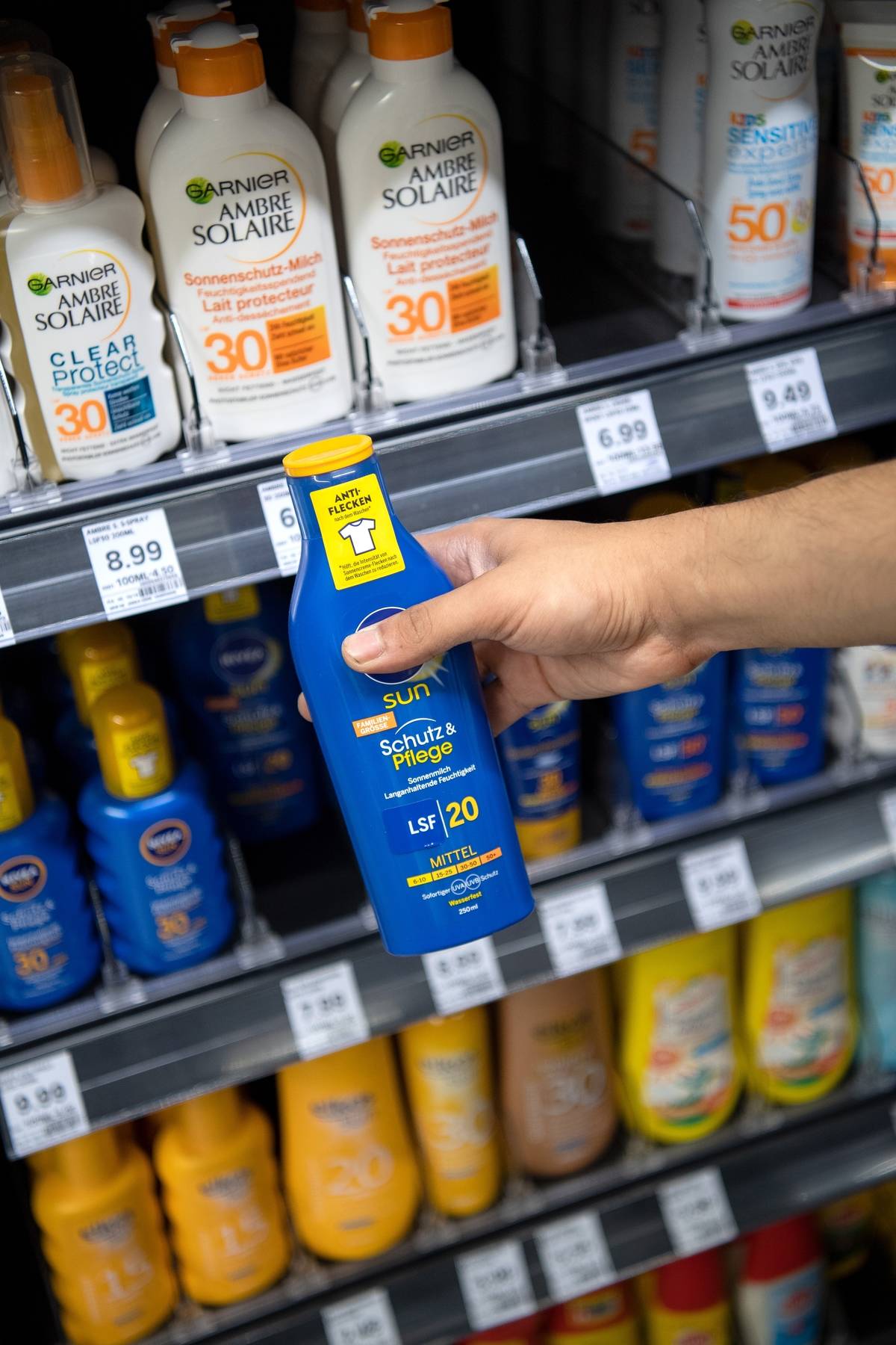 A person chooses a bottle of sunscreen off of a supermarket shelf.