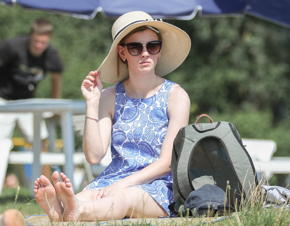 A woman wears a hat and sunglasses while sunbathing.