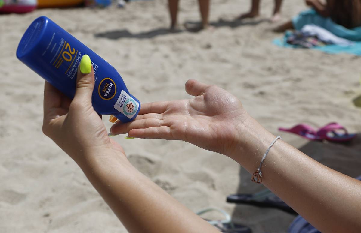 A woman pours sunscreen on her hand at the beach.