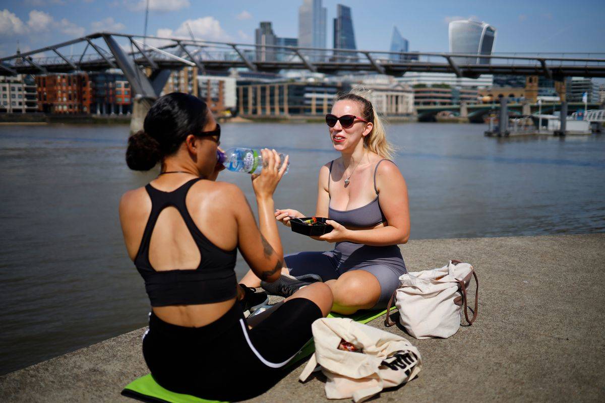 To women eat lunch beside a river outside.