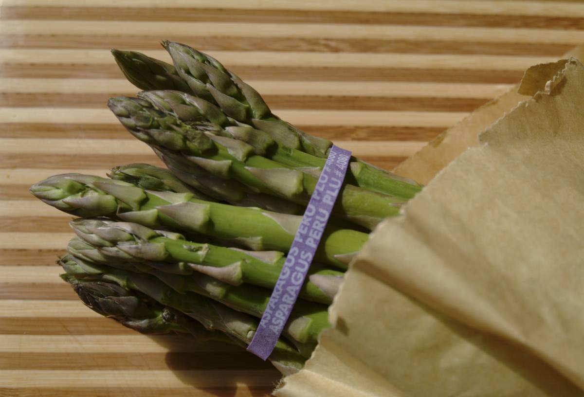 A bunch of asparagus is wrapped in a paper bag.