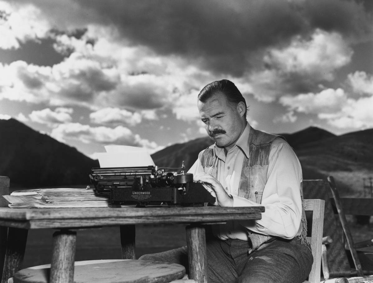 American writer Ernest Hemingway (1899 - 1961) works at his typewriter while sitting outdoors