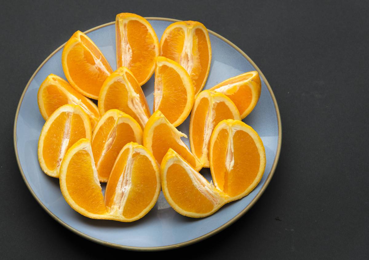 Quarter cut and unpeeled pieces of orange fruit arranged on a round blue plate