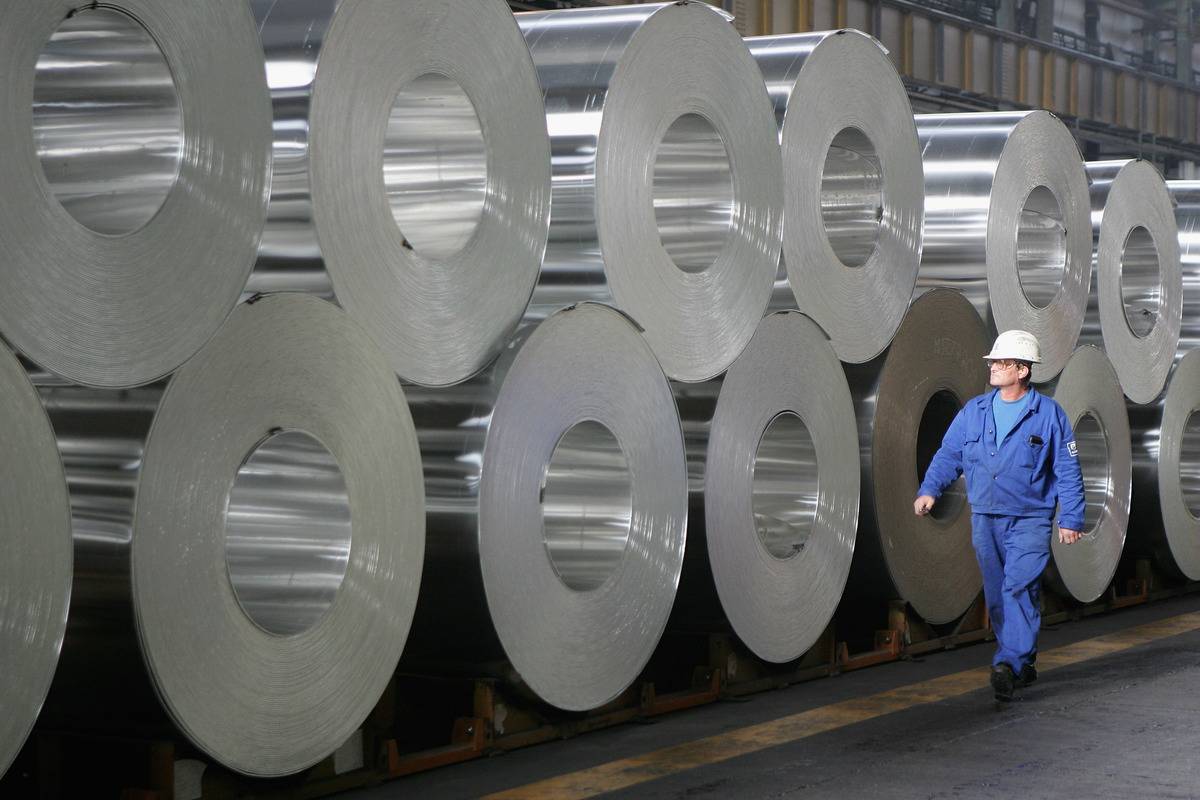 A worker walks among rolls of semi-finished aluminum at the Alcoa aluminum factory