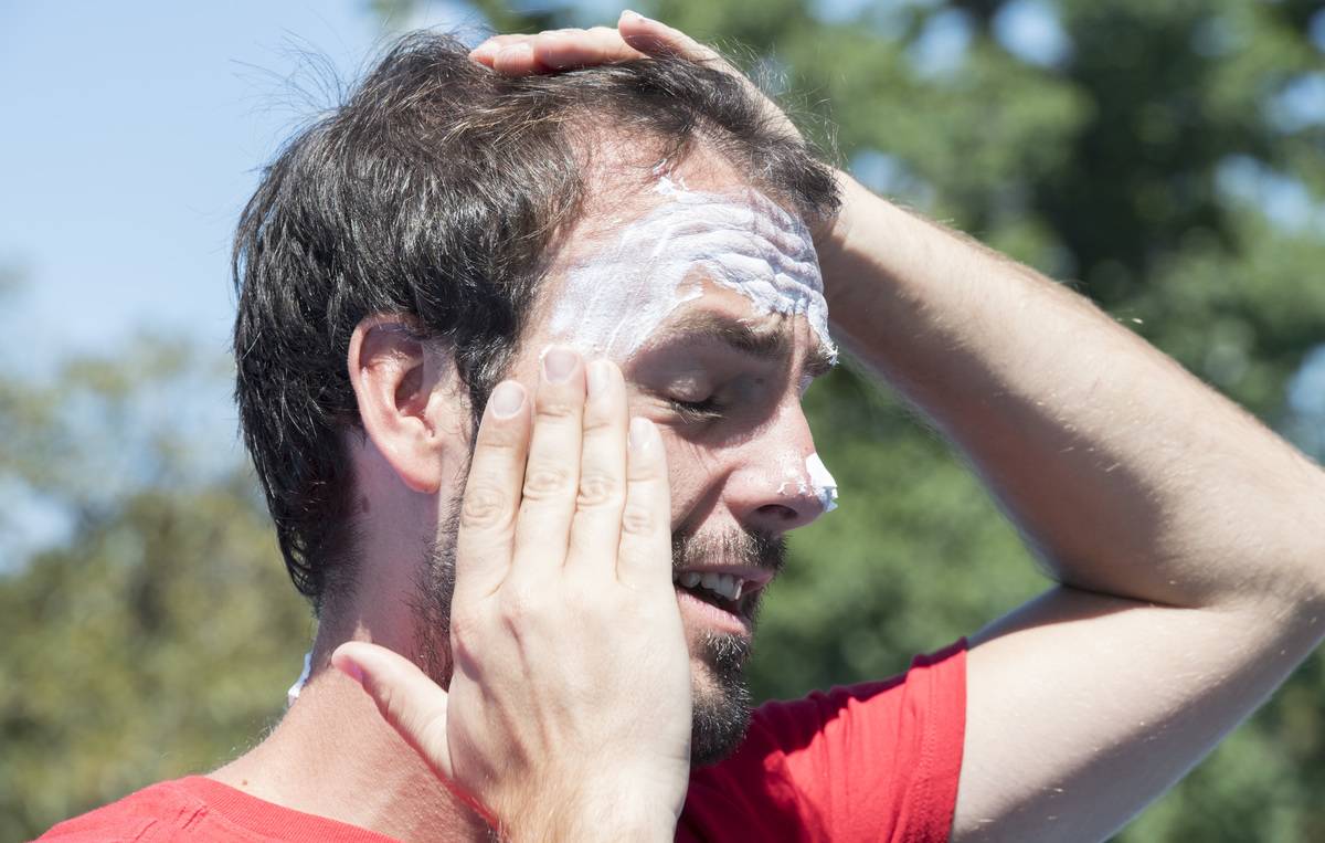 A man rubs sunscreen on his face.