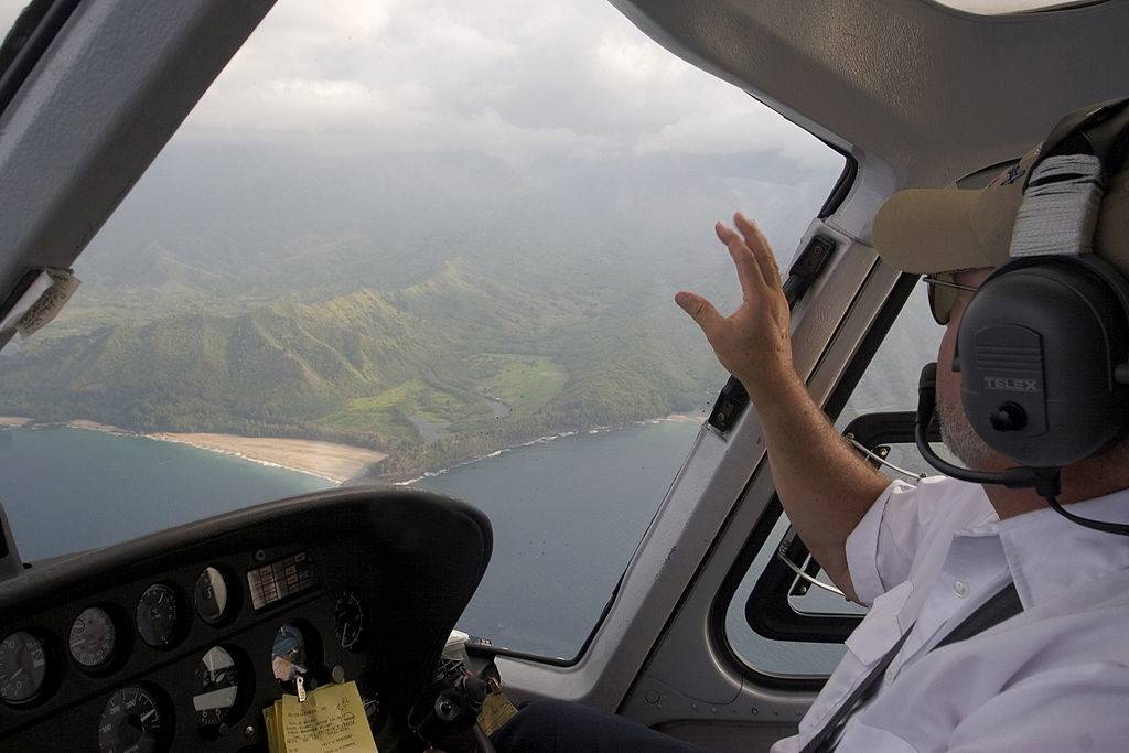 a helicopter pilot looking out onto the green mountains and ocean in kauai from his helicopter