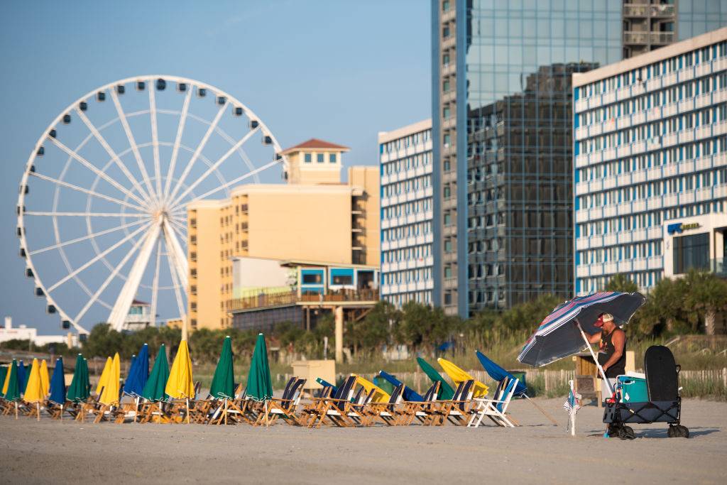 a man putting up an umbrella on a beach with buildings and a ferris wheel in the background in Myrtle Beach, South Carolina