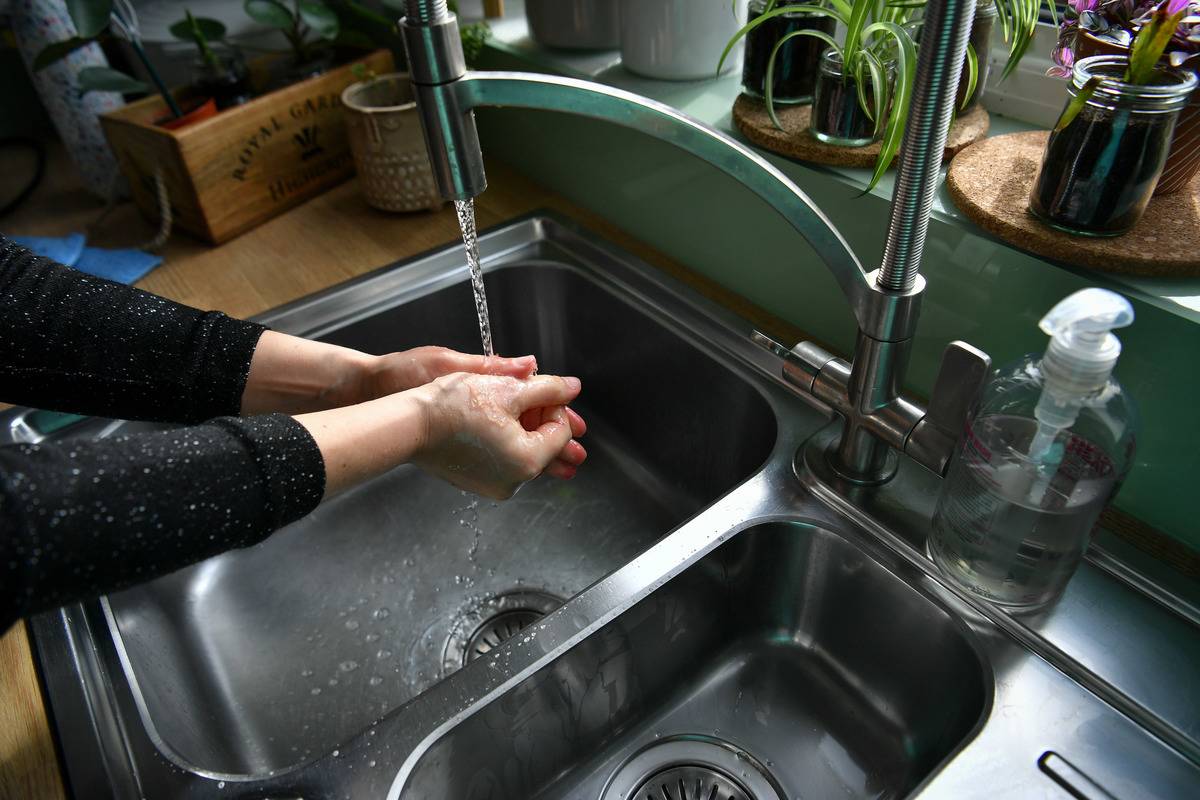 A woman washes her hand in a kitchen sink.