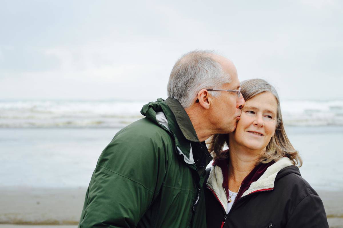 Old man kisses woman by the beach
