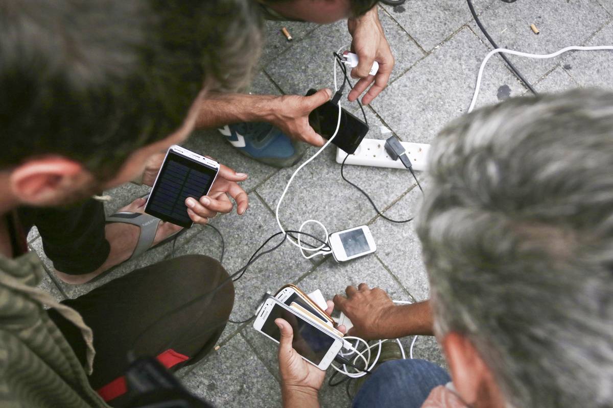 Multiple people charge their iPhones with chargers.
