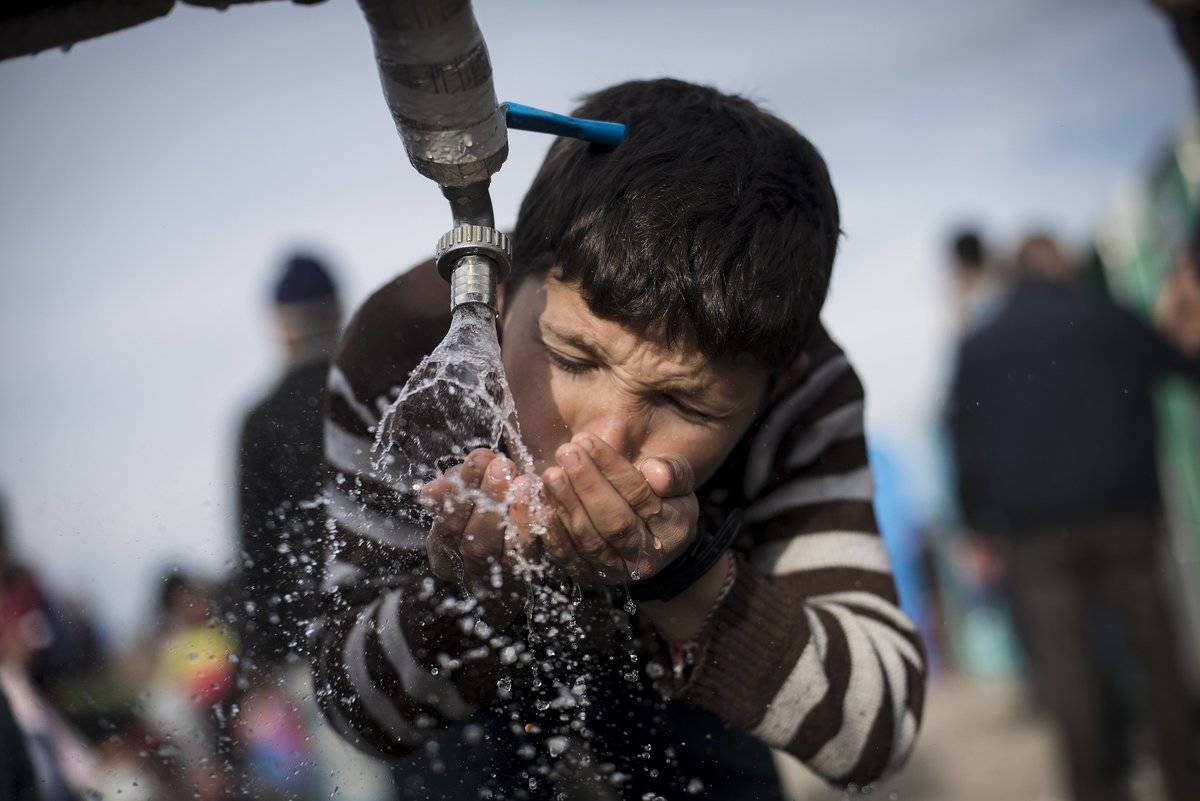 A boy drinks water from a faucet in Greece.