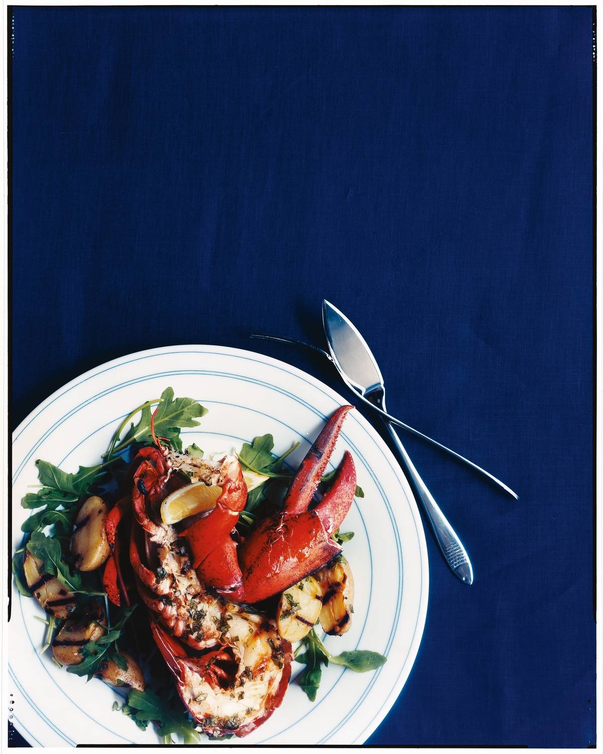 Grilled lobster salad sits on a plate on a blue tablecloth.