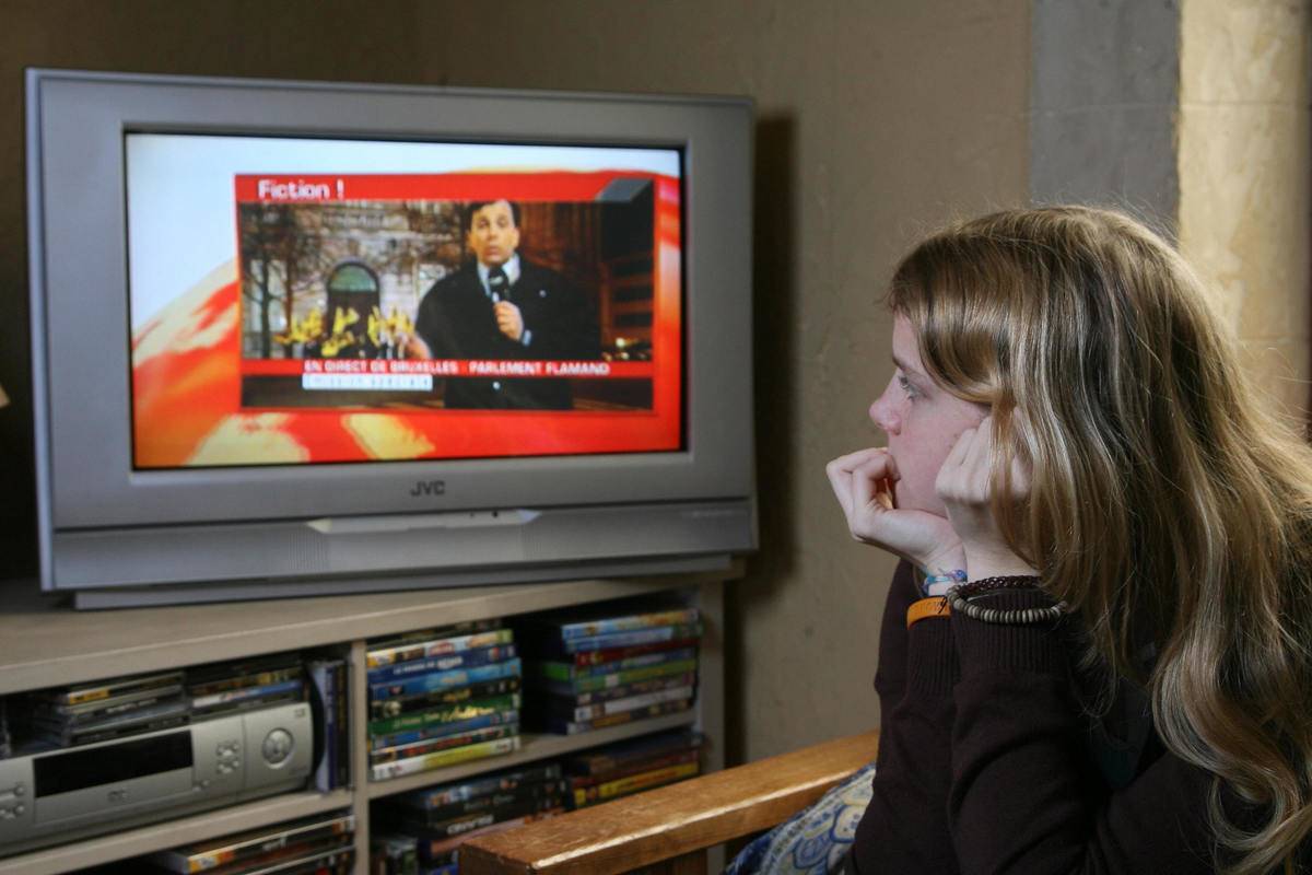 A teenage girl watches the news on TV.