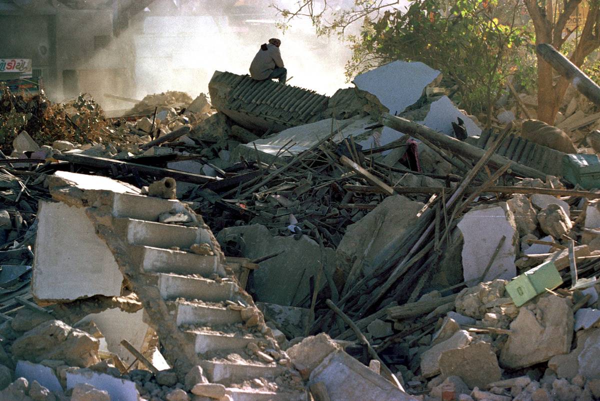 A man sits on top of what used to be his home while watching bulldozers clear the ruins of Old Anjar